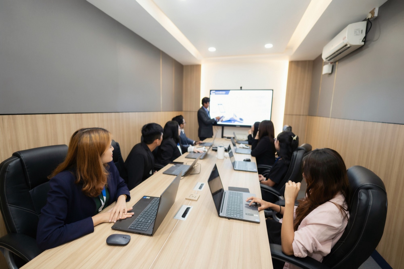 CYNEXIX colleagues with their laptops in a meeting room, watching a presentation on a large screen