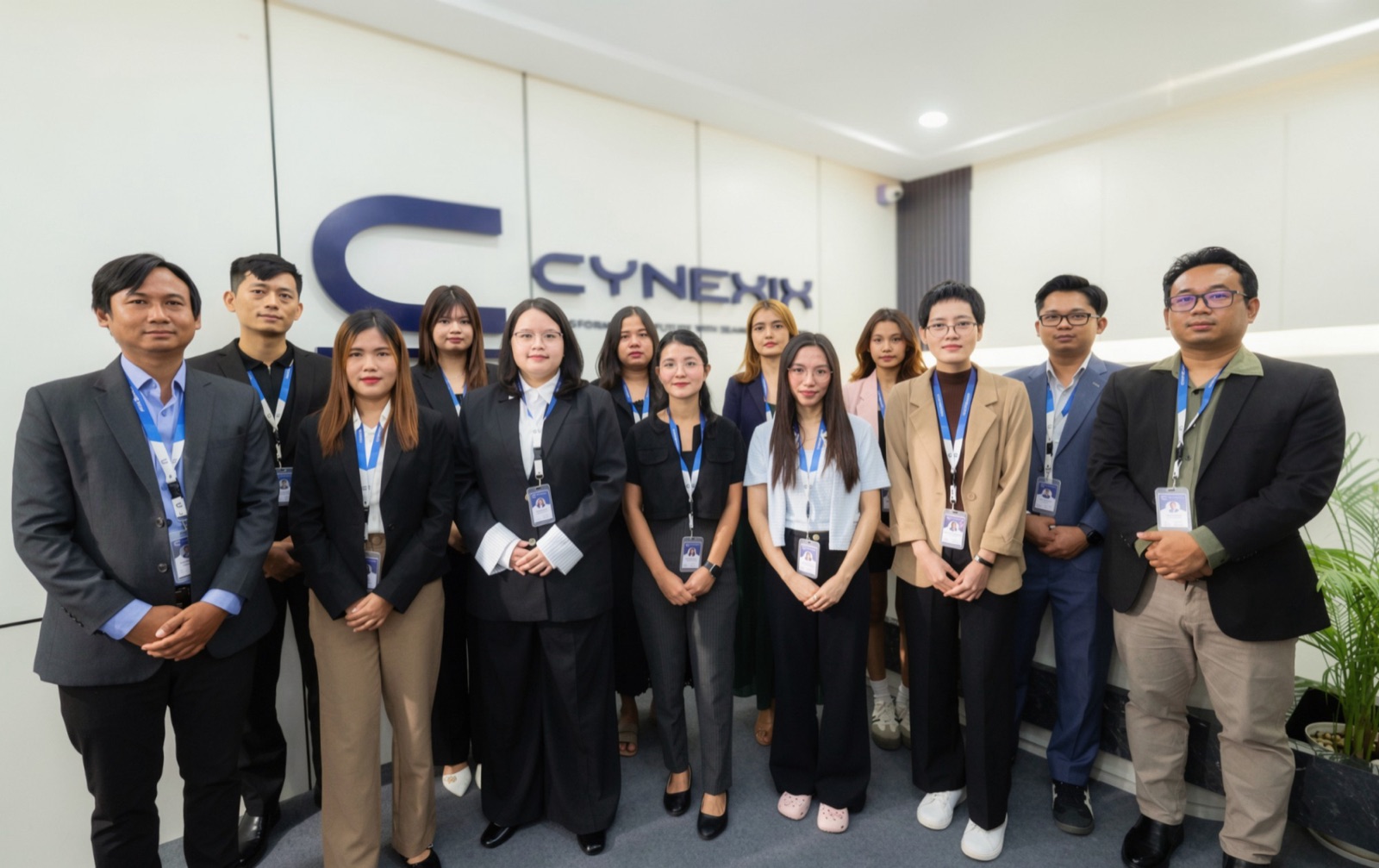 The CYNEXIX team in business attire in front of the logo wall at the office