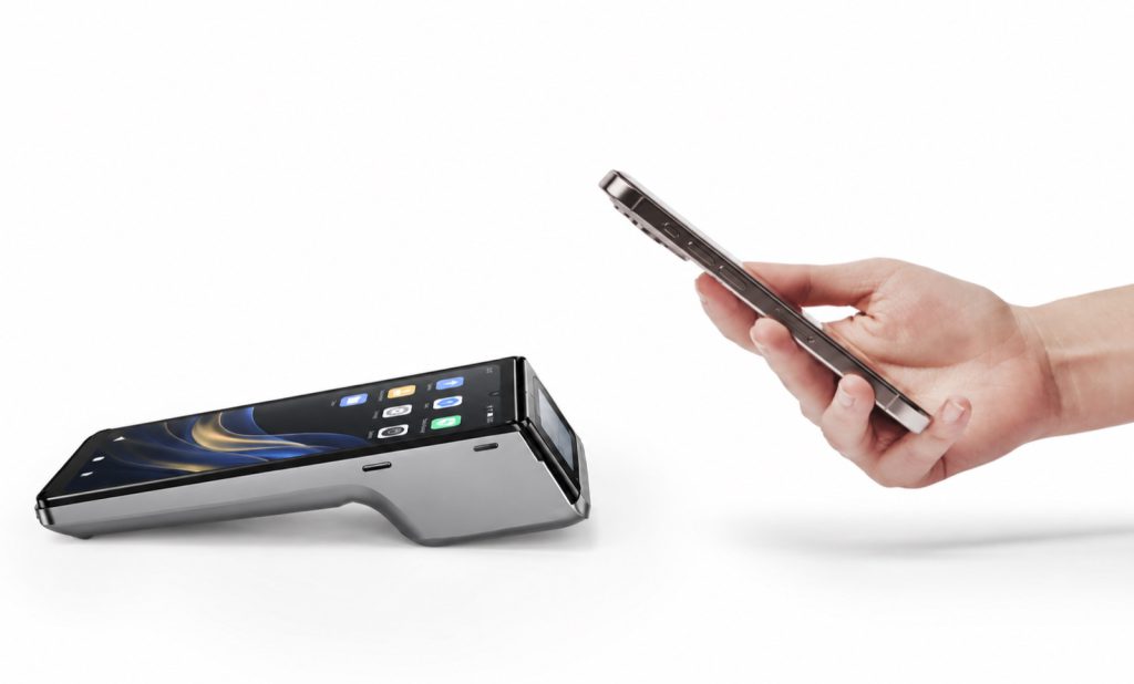 A dual-screen Android POS terminal with the merchant screen and a customer-facing screen, as a customer holds up a phone to pay.